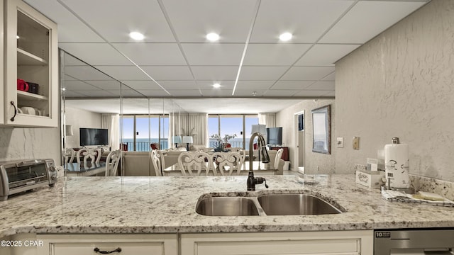 kitchen featuring a sink, dishwasher, light stone countertops, a textured wall, and glass insert cabinets