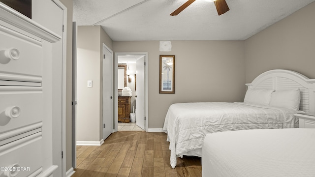 bedroom featuring baseboards, wood finished floors, ensuite bathroom, and ceiling fan