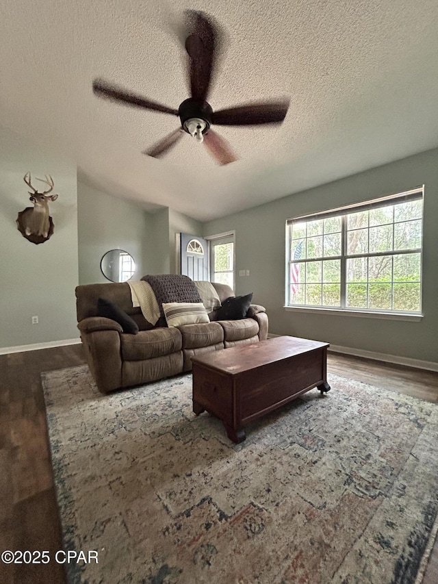 living area featuring baseboards, a textured ceiling, ceiling fan, and wood finished floors