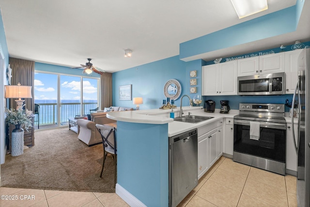 kitchen featuring a peninsula, a sink, stainless steel appliances, open floor plan, and white cabinets