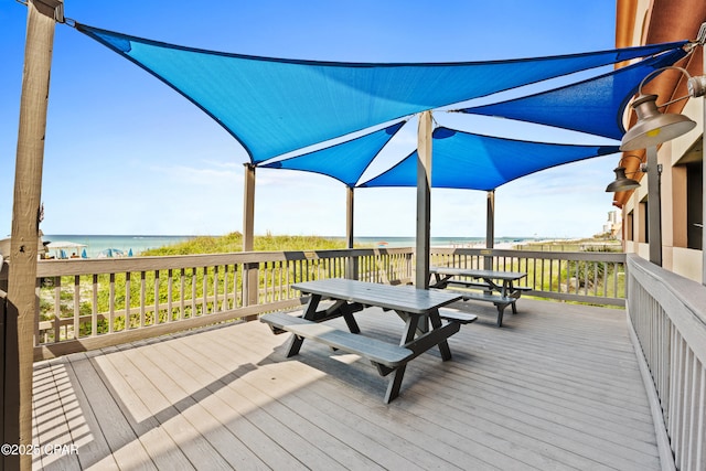 deck featuring a water view, outdoor dining space, and a beach view