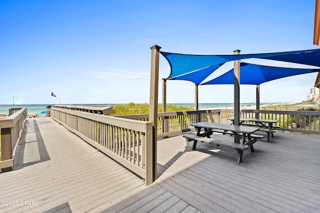 surrounding community with a deck with water view, outdoor dining space, and a view of the beach