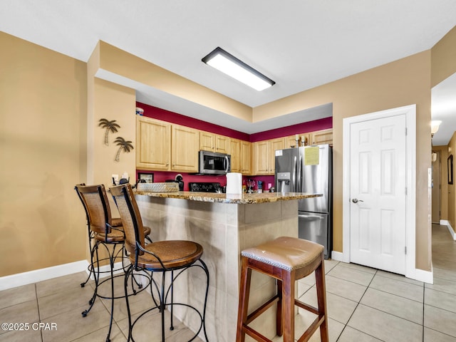 kitchen featuring light tile patterned floors, a breakfast bar, light brown cabinets, appliances with stainless steel finishes, and light stone counters