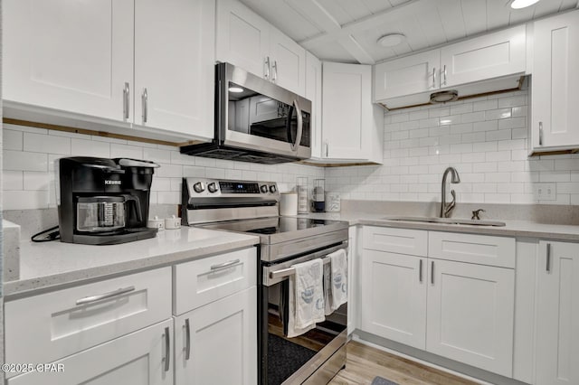 kitchen with stainless steel appliances, a sink, white cabinets, decorative backsplash, and light wood-style flooring