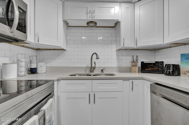 kitchen with appliances with stainless steel finishes, a sink, decorative backsplash, white cabinets, and light countertops