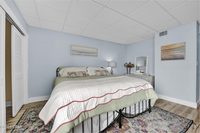 bedroom featuring a paneled ceiling, wood finished floors, baseboards, and a closet