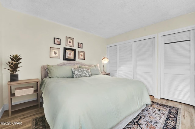bedroom with a textured ceiling, wood finished floors, and multiple closets
