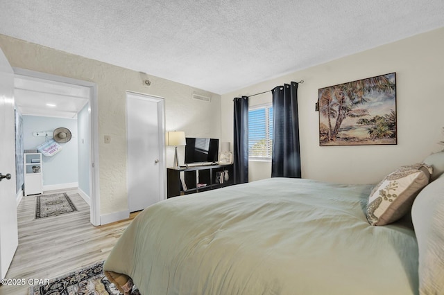 bedroom with wood finished floors, a textured ceiling, and baseboards