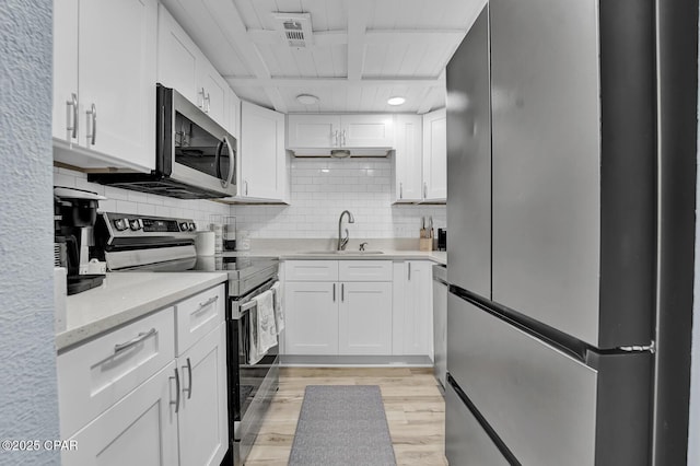 kitchen with stainless steel appliances, a sink, light wood-type flooring, white cabinets, and decorative backsplash