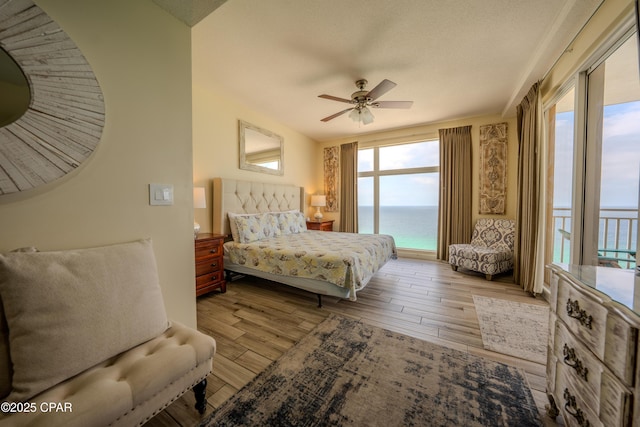 bedroom featuring a water view, wood finished floors, a ceiling fan, and access to outside