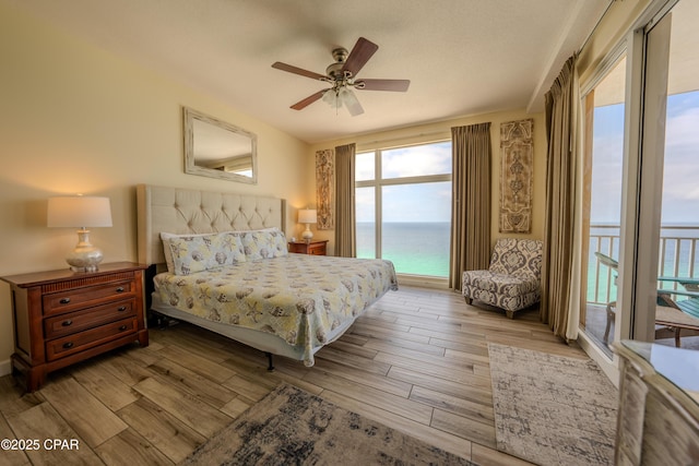 bedroom with a water view, access to outside, light wood-style flooring, and ceiling fan