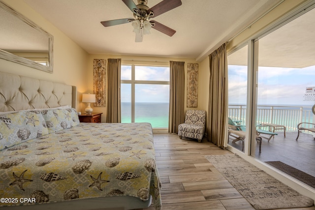 bedroom with light wood finished floors, a water view, access to outside, and a ceiling fan