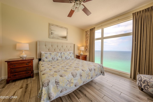 bedroom featuring a water view, a ceiling fan, and wood finished floors
