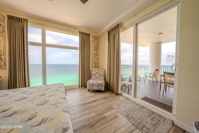bedroom with light wood finished floors, a water view, and access to outside