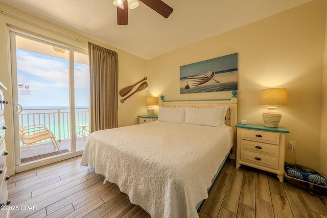 bedroom featuring a ceiling fan, a water view, access to exterior, and wood-type flooring