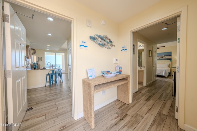 hallway featuring light wood finished floors, baseboards, and recessed lighting