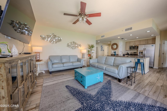 living room featuring light wood finished floors, ceiling fan, and visible vents