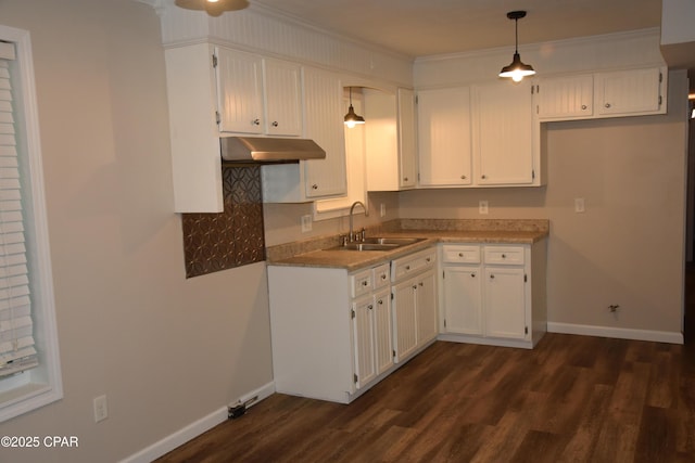 kitchen with a sink, white cabinetry, dark wood-style floors, baseboards, and ornamental molding