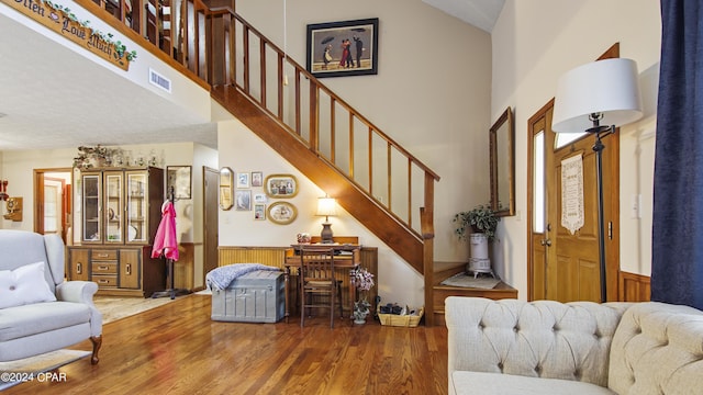 foyer entrance with wood finished floors, high vaulted ceiling, visible vents, stairway, and wainscoting