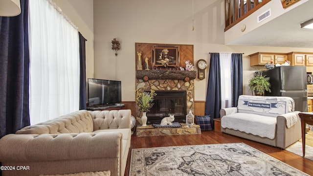 living area featuring wood finished floors, a wainscoted wall, visible vents, a towering ceiling, and a stone fireplace