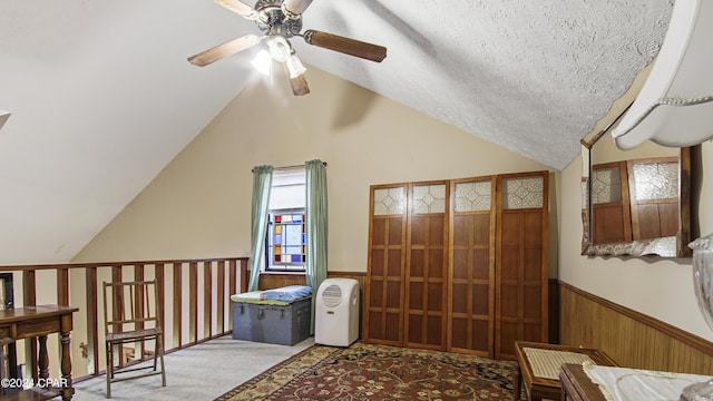 additional living space with a ceiling fan, lofted ceiling, a wainscoted wall, carpet floors, and wood walls