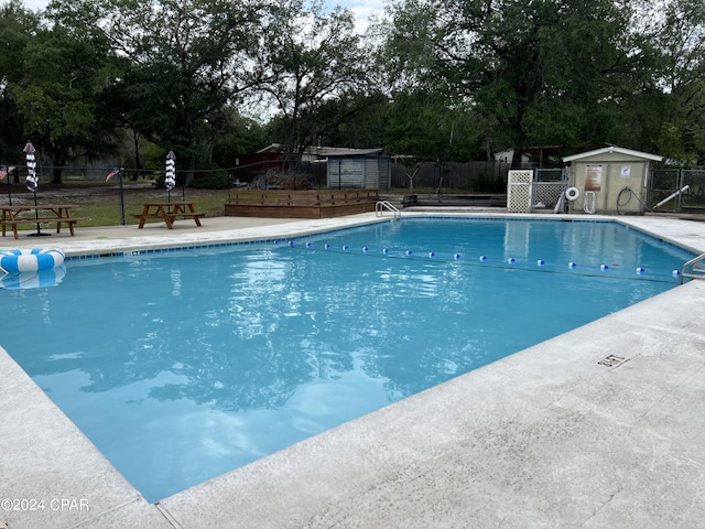 community pool featuring fence, a shed, an outdoor structure, and view of scattered trees