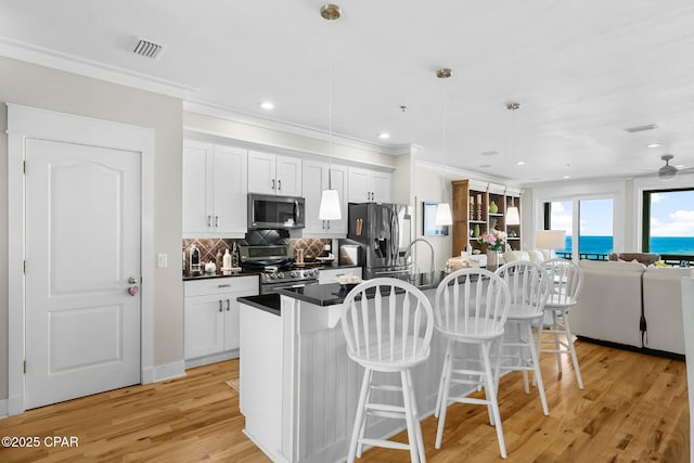 kitchen with appliances with stainless steel finishes, a breakfast bar, dark countertops, a kitchen island with sink, and open floor plan