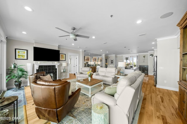 living area with ornamental molding, ceiling fan, recessed lighting, light wood finished floors, and a fireplace