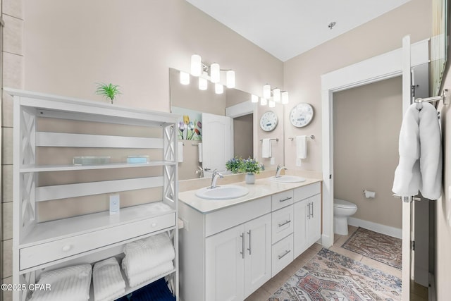 full bath with toilet, tile patterned floors, double vanity, and baseboards