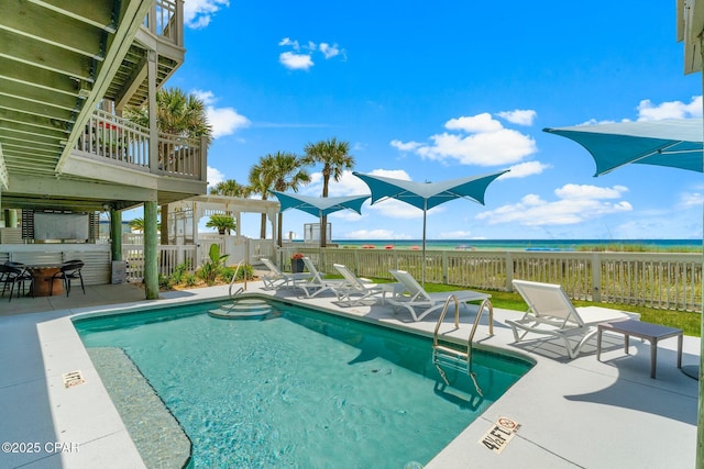 community pool with a jacuzzi, fence, a patio area, and a water view