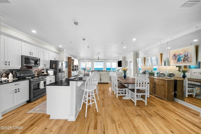 kitchen with appliances with stainless steel finishes, dark countertops, ornamental molding, open floor plan, and light wood finished floors