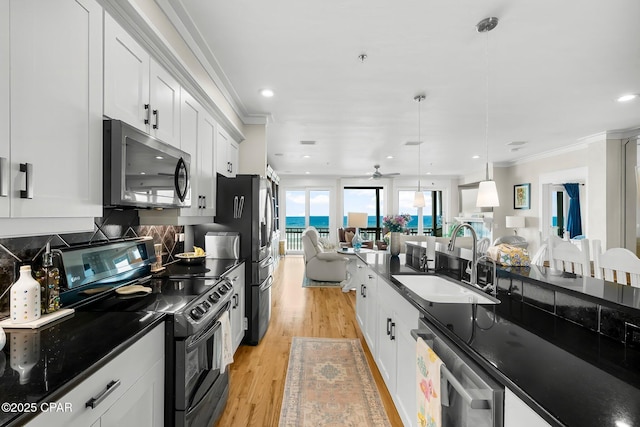 kitchen with appliances with stainless steel finishes, a sink, open floor plan, ornamental molding, and dark countertops