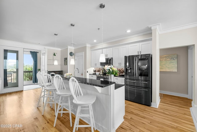 kitchen with appliances with stainless steel finishes, a kitchen bar, ornamental molding, light wood-type flooring, and a center island with sink