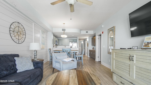 living area featuring light wood-style flooring, a ceiling fan, and baseboards