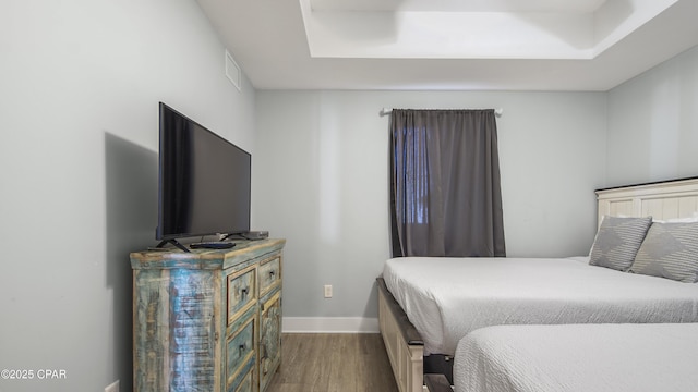 bedroom featuring wood finished floors, baseboards, and a tray ceiling