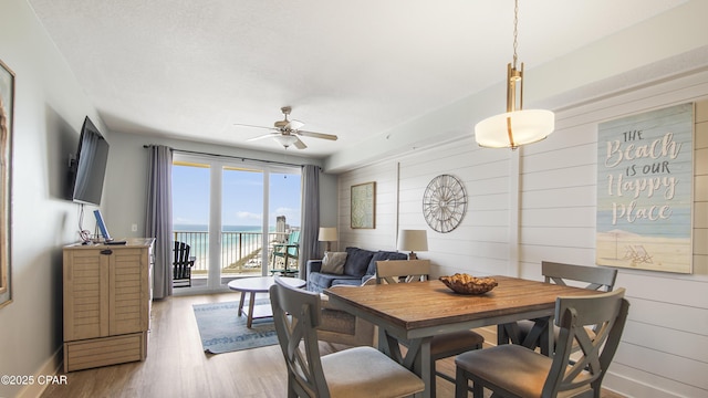 dining area featuring ceiling fan, wood finished floors, wooden walls, and baseboards