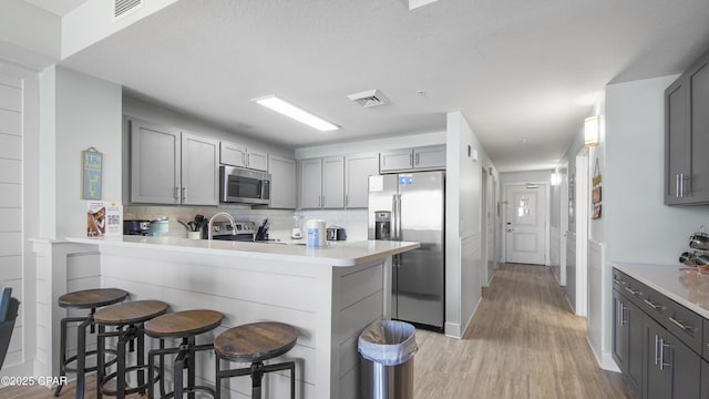 kitchen with stainless steel appliances, gray cabinets, a peninsula, and light wood-type flooring