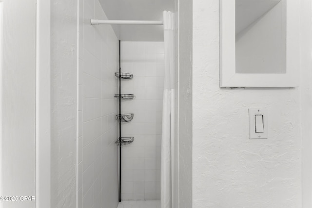 bathroom featuring a textured wall and a tile shower