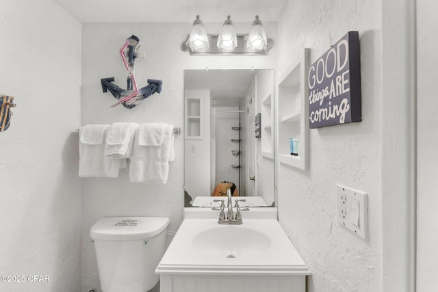 bathroom featuring toilet, a textured wall, and vanity