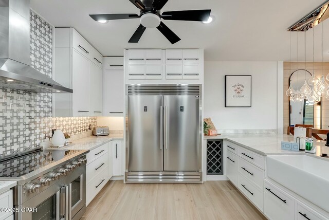 208 George C Wallace, Panama City Beach, FL 32413 - kitchen featuring appliances with stainless steel finishes, wall chimney range hood, light wood finished floors, white cabinetry, and a sink
