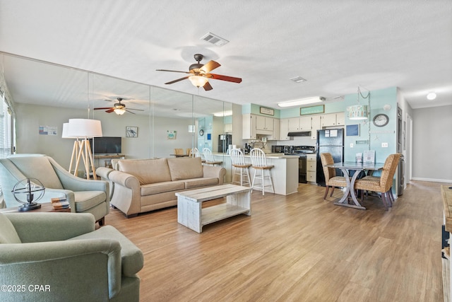 living room featuring light wood-style flooring, ceiling fan, and baseboards