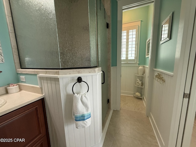 full bath with wainscoting, tile patterned flooring, a stall shower, and vanity