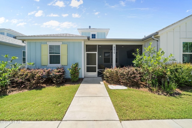 8676 Coral Reef Way, Panama City Beach, FL 32413 - view of front of house featuring board and batten siding, a front yard, and a sunroom