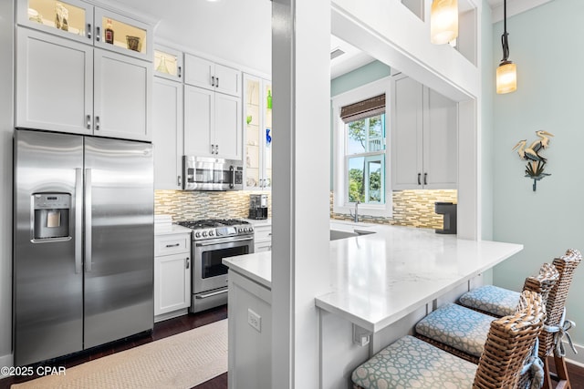 kitchen featuring appliances with stainless steel finishes, backsplash, a breakfast bar area, glass insert cabinets, and decorative light fixtures