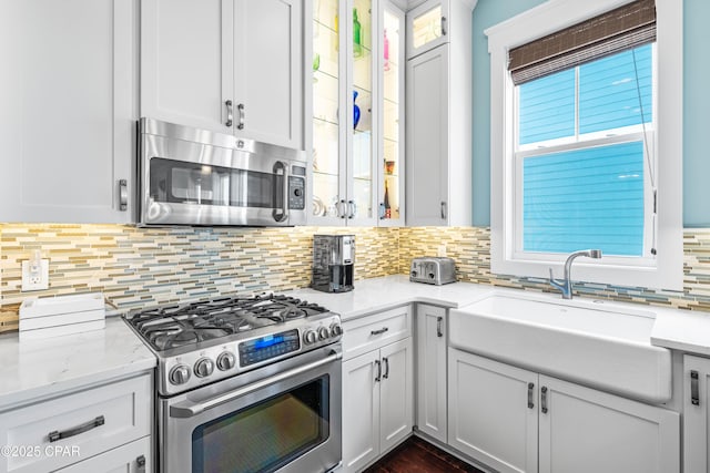 kitchen with stainless steel appliances, a sink, backsplash, glass insert cabinets, and white cabinets