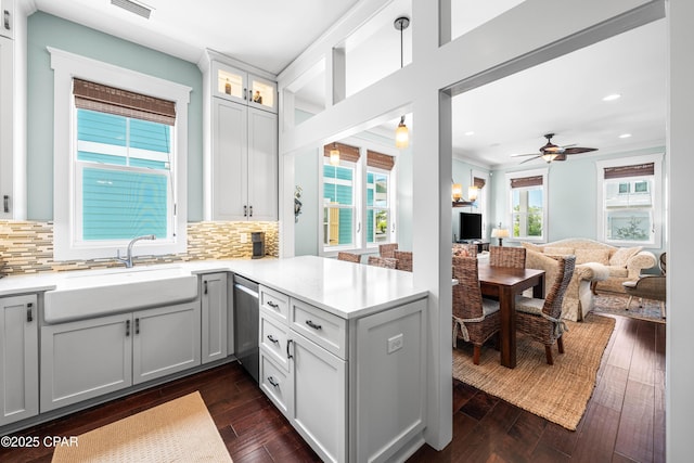 kitchen with a sink, open floor plan, stainless steel dishwasher, a peninsula, and light countertops