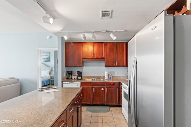 kitchen with white appliances, a sink, rail lighting, light stone counters, and light tile patterned floors