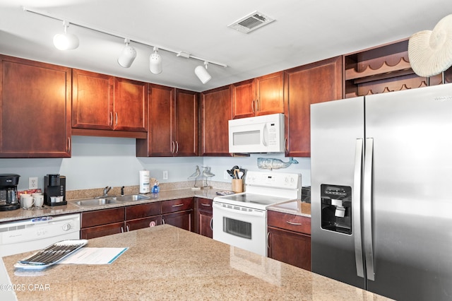 kitchen featuring white appliances, a sink, rail lighting, and light stone counters