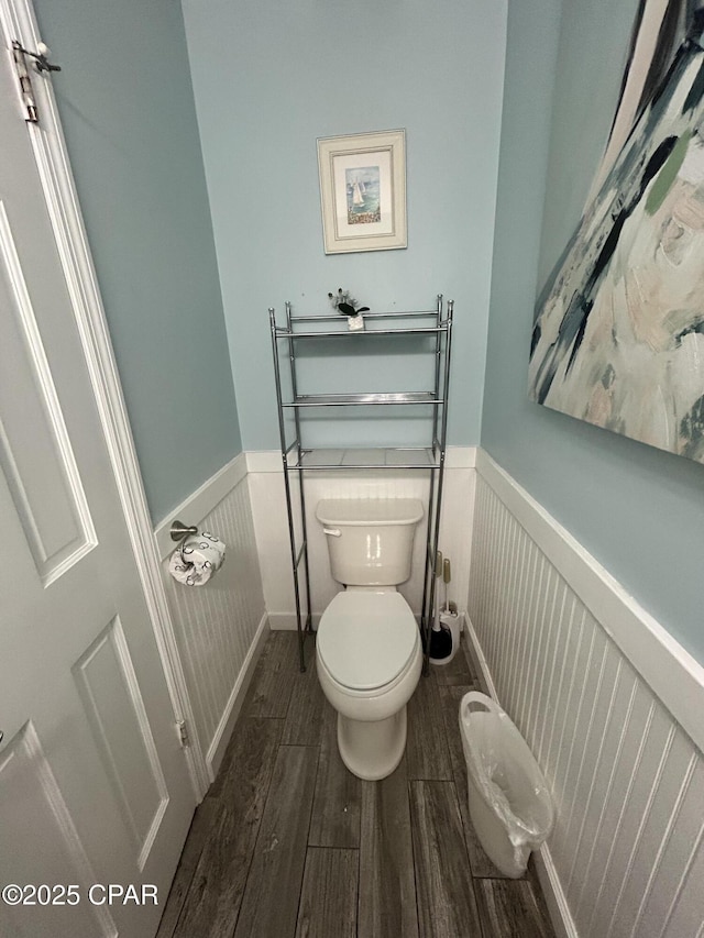 half bathroom with wainscoting, toilet, and wood finished floors