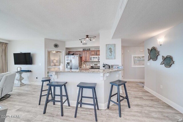 17757 Front Beach Rd Unit 2201A, Panama City Beach, FL 32413 - kitchen featuring stainless steel appliances, a textured ceiling, brown cabinetry, a breakfast bar, and light wood-style floors